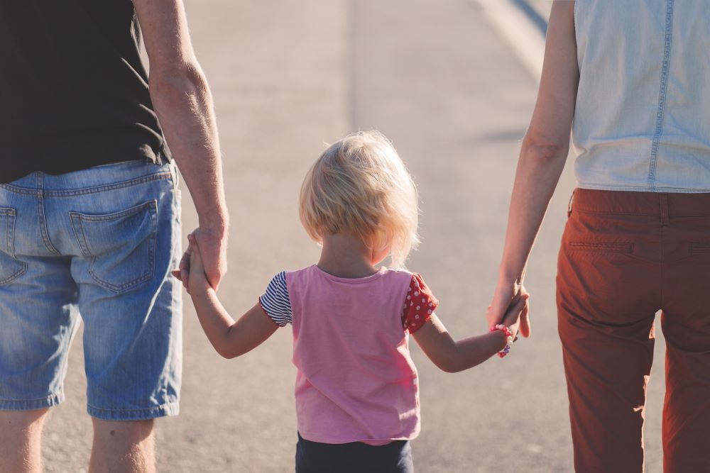 A young child is holding the hand of a man and woman