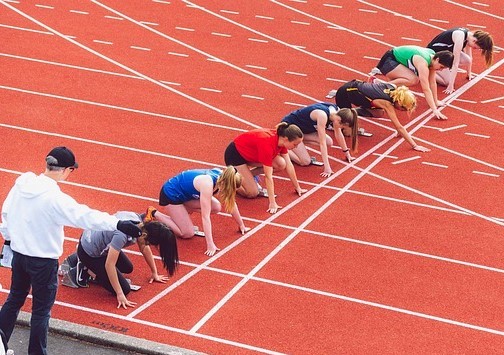 Young people at the start line on a race track with a teacher or coach beside them.